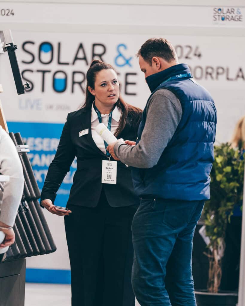 A woman in a black suit and a man in a blue vest engage in conversation at a booth, captured by an event photographer. The sign behind them reads Solar & Storage Live, reflecting the professional atmosphere of the conference.